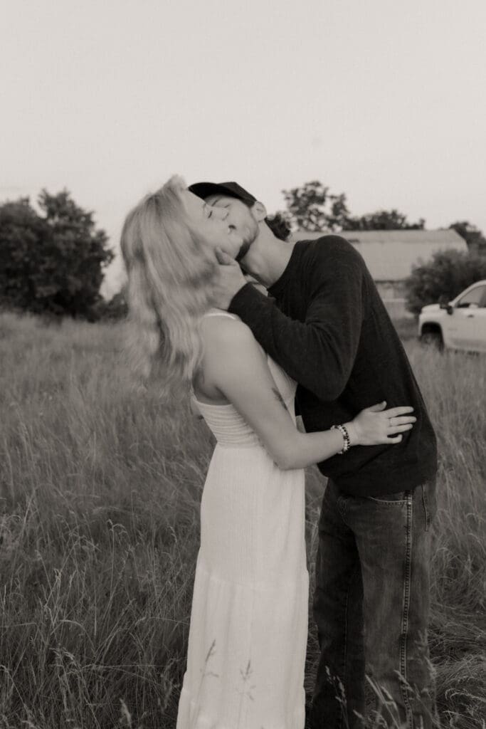 A black and white image of a couple kissing in a field.
