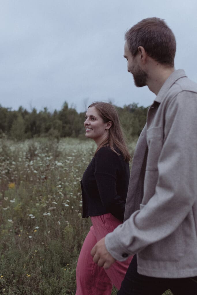 An engaged couple walking through a field in Kemptville, Ontario.